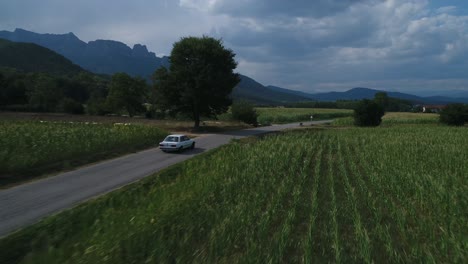 Aerial-drone-of-a-countryside-landscape,-isolated-classic-car-driving-fast