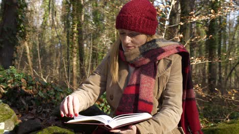 Woman-reading-book-in-forest-wearing-winter-scarf-and-hat,-Mid-Shot-Orbit