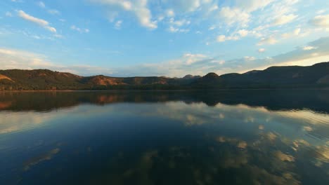 Panning-over-a-still-freshwater-lake,-showing-a-perfect-reflection-of-the-hills-and-blue-sky