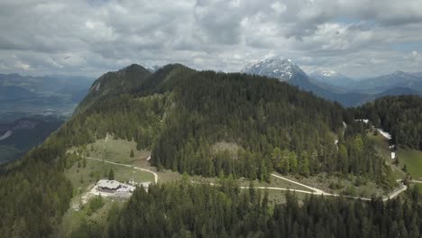 Luftaufnahme-Von-Hütten-Auf-Einem-Wunderschönen-Berggipfel-Mit-Einer-Schneebedeckten-Bergkette-Im-Hintergrund