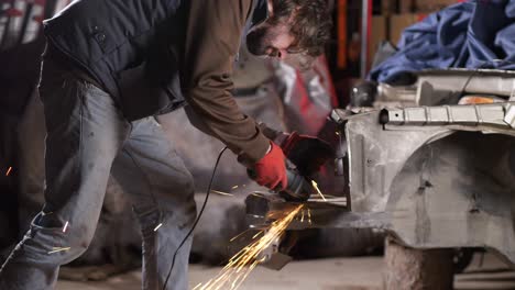 Mechanic-man-uses-sparking-circular-saw-on-metal-bodywork-of-car-in-workshop