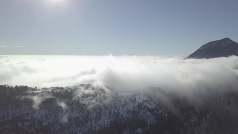 Aerial-view-of-clouds-rolling-over-a-snowy-mountain-range