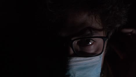 Nahaufnahme-Bärtiger-Mann-Mit-Koronavirus-OP-Maske,-Der-Im-Dunkeln-Auf-Die-Kamera-Blickt