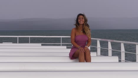 Girl-In-Dress-Sitting-On-Deck-Smiling-At-Camera-While-Hair-Blowing-In-The-Wind---Girl-At-Ferry-Deck-Cruising-In-The-Ocean
