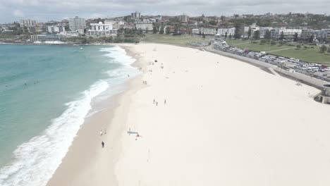 People-Walk-At-White-Sand-Of-Bondi-Beach-In-Summer---Bondi-Beach-Lifeguard-Tower-And-Parking-Lot---NSW,-Australia