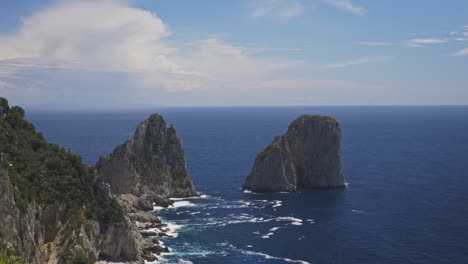 Small-boats-pass-near-Faraglioni-in-Capri-during-a-sunny-day,-Timelapse