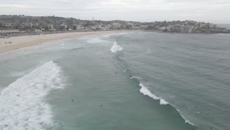 Flying-Towards-Blue-Ocean-With-Surfers-On-Rolling-Waves-At-Bondi-Beach-In-Eastern-Suburbs,-Sydney,-NSW-Australia