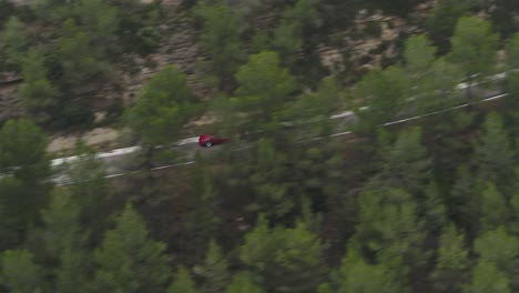Speeding-Red-Car-On-Curvature-Road-Passing-By-Dense-Trees-Near-Barcelona,-Spain
