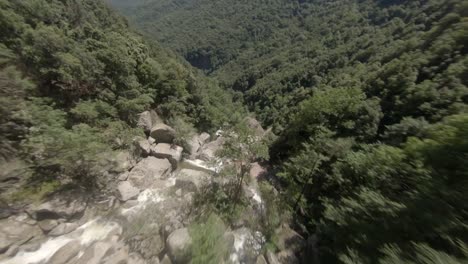 Unique-fpv-drone-flight-alongside-a-waterfall-down-a-rocky-ravine-in-a-green-forest