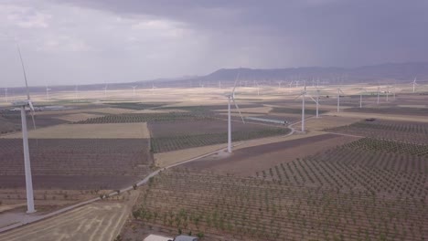 Spinning-sustainable-renewable-energy-wind-turbines-aerial-view-across-farmland-meadow-landscape-Spain