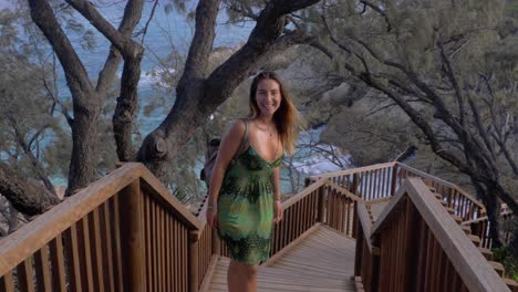 Young-Woman-Standing-At-Wooden-Stairs-In-North-Gorge-Walk-Turn-Around-And-Smiled-Happily---Ocean-View-Behind-Trees-In-Point-Lookout,-QLD,-Australia