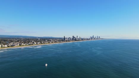 Aerial-View-Of-Sailboat-In-Calm-Blue-Sea-Near-Miami-Coastal-Suburb---Skyline-Of-Broadbeach-And-Surfers-Paradise-In-Gold-Coast,-QLD,-Australia