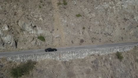 Dark-car-travelling-along-long-coastal-route-1-California-state-road-aerial-tracking-view-following-journey