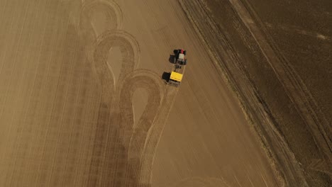 Tracking-aerial-view-of-a-red-double-wheeled-tractor-with-yellow-seeder-finished-sowing-seeds-and-parking-the-tractor-between-two-agricultural-fields