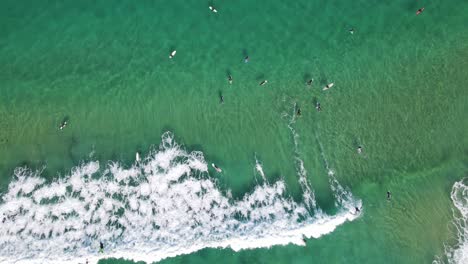 Top-View-Of-Surfers-On-Bright-Blue-Ocean-Surface-With-Waves-Splashing