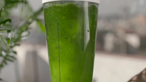 Nutritious-juicy-green-fruit-smoothie-spinning-slow-motion-in-blender-on-sunny-balcony