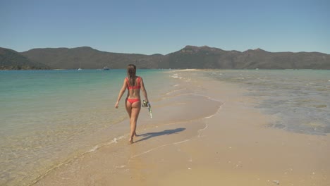 Female-Tourist-In-Bikini-Holding-Snorkeling-Equipment-While-Walking-On-The-Sand-Bridge-Of-Langford-Island-In-Whitsundays,-Queensland-At-Summer