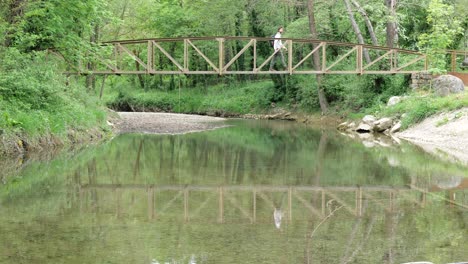 Static-locked-off-shot-of-a-man-walking-over-a-bridge-reflecting-in-a-small-river-in-Catalonia-Spain