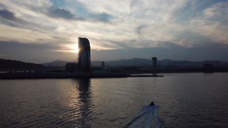 Ein-Schnelles-Kleines-Boot-Betritt-Barcelona-Bei-Sonnenuntergang-Mit-Schöner-Silhouettierter-Skyline-Im-Hintergrund