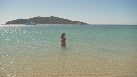 Lady-in-an-orange-bikini-standing-in-shallow-water,-admiring-the-view--Langford-Island,-Australia