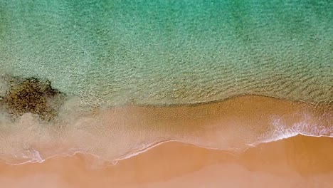 Aerial:-birds-eye-view-of-crystal-blue-water,-waves-on-shore