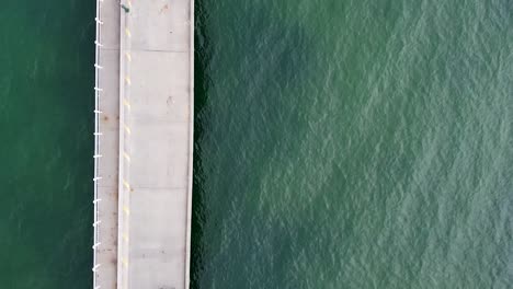 Aerial---birds-eye-drone-shot-of-couple-walking-along-bridge-over-green-water
