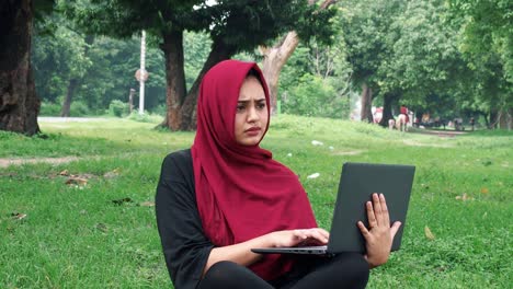 Happy-Afghan-woman-in-hijab-working-on-laptop-computer-on-green-lawn-near-busy-road