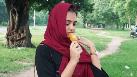 Schöne-Junge-Afghanische-Frau-Im-Hijab,-Die-Auf-Dem-See-Steht-Und-Eis-Mit-Orangengeschmack-Isst
