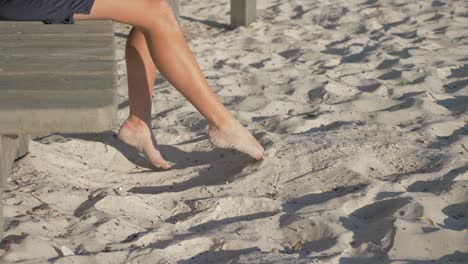 Person-Sitzen,-Die-Füße-Schwingen-Und-Mit-Dem-Sand-Spielen---Sommerferien