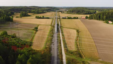 High-altitude-tracking-aerial-drone-view-of-high-speed-passenger-train-traveling-on-long-straight-track-passing-under-multilane-highway-bridge-with-fields-and-forests-on-both-sides