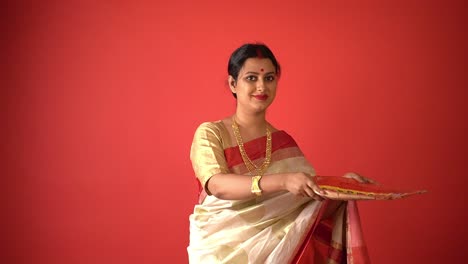 Porträt-Einer-Schönen-Bengalischen-Frau-In-Rot-weißem-Saree-Auf-Rotem-Hintergrund,-Die-Lächelt,-Während-Sie-Einen-Handgefertigten-Teller-Hält