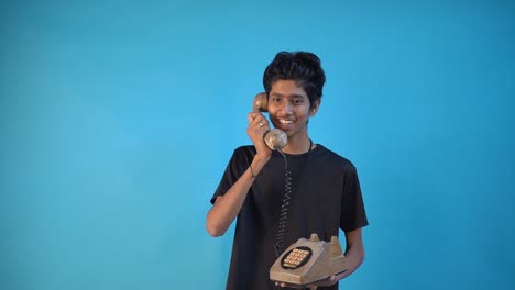 Happy-excited-young-Indian-guy-20s-years-old-in-black-t-shirt-hold-using-old-telephone-just-found-out-great-big-win-news-isolated-on-pastel-blue-background-studio