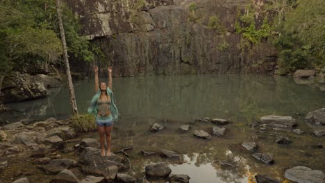 Girl-With-Scarf-Standing-On-Rock-And-Raising-Hands-in-The-Air---Cedar-Creek-Falls-In-QLD,-Australia