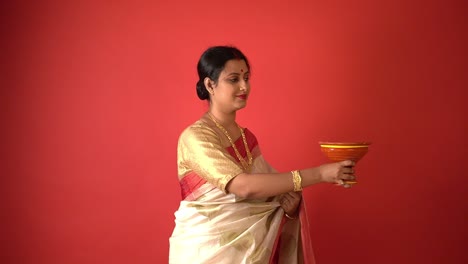 A-Indian-Bengali-woman-wearing-white-saree-with-dhoop-cup-in-red-background-studio