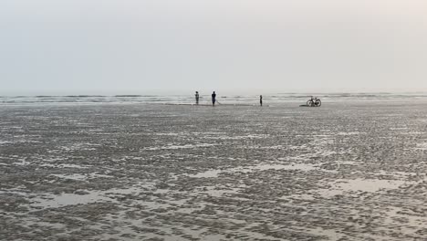 Distant-silhouette-view-of-an-empty-beach-with-fishermen-working-on-fishing-net-and-cycle-parked-aside-in-Bengal,-India