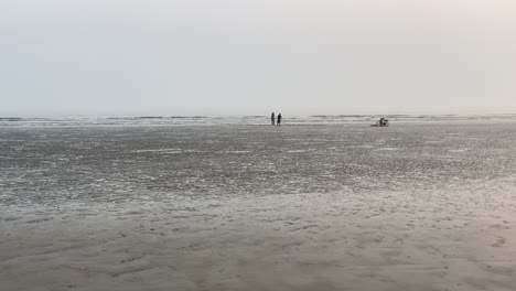 POV-Walking-Shot-Eines-Leeren-Strandes-Mit-Einem-Fischer-Und-Seinem-Einzigen-Sohn,-Die-Vor-Meereswellen-An-Ihrem-Fischernetz-Arbeiten