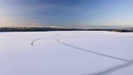 Forward-moving-ascending-aerial-view-over-frozen-lake-with-natural-line-patterns-on-ice,-revealing-beautiful-winter-forest-around-the-lake