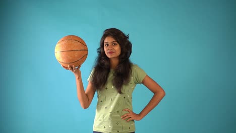 A-young-Indian-girl-in-green-t-shirt-seeing-the-camera-standing-with-basketball-in-an-isolated-blue-background-studio