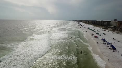 Sandy-Beach-With-Tourists-Enjoying-Summer-Holidays-At-Orange-Beach-On-The-Gulf-Of-Mexico-In-Alabama-On-A-Cloudy-Day---aerial-drone-shot