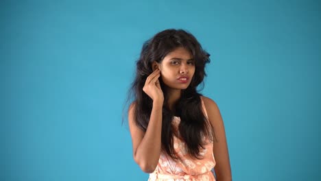 A-young-Indian-girl-in-orange-frock-giving-'What'-expression-in-an-isolated-blue-background