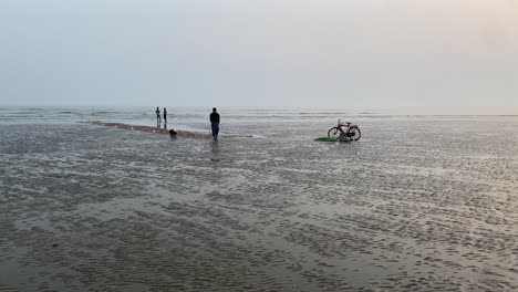 Silhouette-Gimble-Aufnahme-Eines-Angenehmen-Abends-Am-Strand-In-Indien-Mit-Einem-Fischer,-Der-In-Der-Nähe-Seines-Fahrrads-Steht-Und-An-Seinem-Netz-Arbeitet