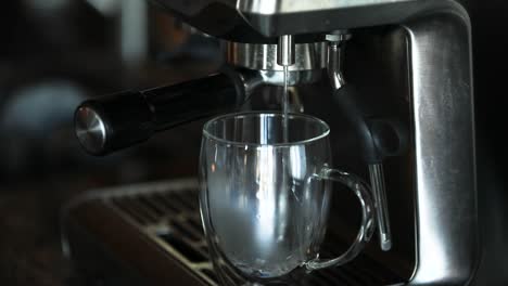 Man-turning-a-switch-on-an-automatic-espresso-machine-to-pour-steaming-hot-water-into-a-see-through-glass-cup