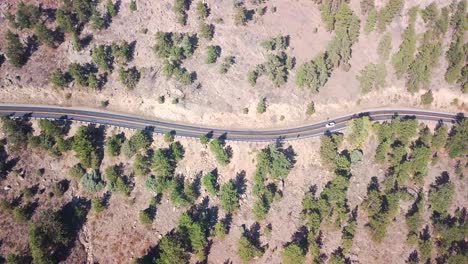 Stand-still-aerial-shot-of-a-car-driving-up-the-hill-on-a-winding-mid-western-road-in-the-mountains-with-pine-trees