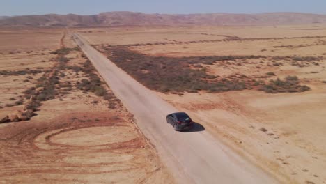 Black-touring-car-merging-onto-long-road-in-vast-orange-desert