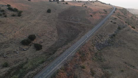 Aerial-drone-view-tracking-a-car-driving-up-the-highlands-of-Golan-Heights,-in-Israel