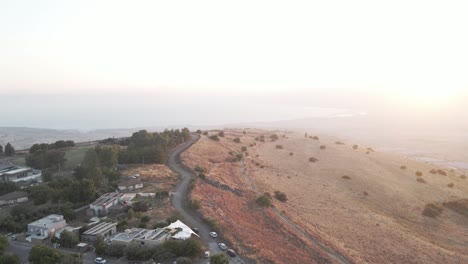 Aerial-view-overlooking-houses-and-a-road-in-the-highlands-of-Golan-Heights,-sunset-in-Israel---ascending,-tilt,-drone-shot