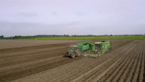 Grüner-Traktor-Auf-Braunem-Feld-Mit-Grünem-Feld-Und-Wald-Im-Hintergrund-4k-Drohne