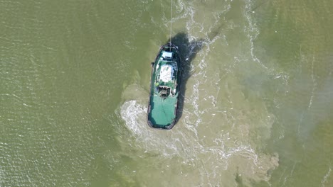 Aerial-top-down-view-of-tugboat-manoeuvring-in-shallow-waters-disturbing-bottom-sediment