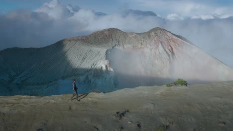 Man-adventure-hiking-along-cliff-ridge-at-active-volcano-in-East-Java,-profile-shot,-aerial