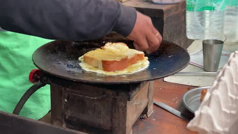 Un-Hombre-Cocinando-Tostadas-De-Pan-Mezcladas-Con-Huevos-En-Una-Sartén-De-Acero-Caliente-Con-Aceite-De-Trigo-Hervido-Mezclando-Aceite-De-Mantequilla,-Concepto-De-Comida-Callejera-En-India